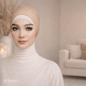 Könnte beinhalten: Eine Frau trägt einen beigefarbenen Hijab und einen weißen Rollkragenpullover. Der Hijab bedeckt Kopf und Hals, mit einem weißen Band um die Stirn. Das Bild hat eine weiche, neutrale Farbpalette.