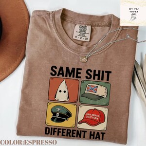以下が含まれることがあります： 「SAME SHIT DIFFERENT HAT」の文字と4つの異なる帽子の画像がプリントされたエスプレッソカラーのTシャツ。TシャツにはComfort Colorsのラベルとネックレスが付いています。