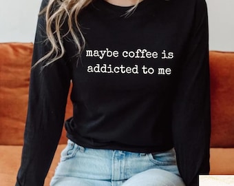 May include: Black long-sleeve shirt with the white text "maybe coffee is addicted to me". The shirt is paired with blue jeans. The shirt is made of a soft, comfortable material.