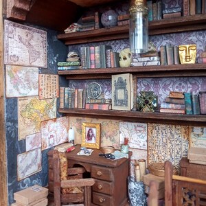 May include: Miniature library scene with a desk, chair, and bookshelves filled with tiny books. The walls are adorned with maps and framed artwork. A hanging light fixture and decorative objects complete the detailed interior.
