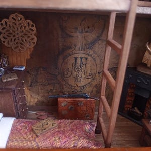 May include: Miniature diorama of a room with a bed, dresser, and fireplace. The walls are decorated with a map-like design and a large emblem. A small wooden ladder leads to a second level. A decorative piece hangs on the wall.