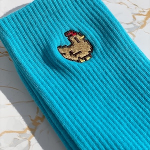 May include: A pair of turquoise blue socks with a small embroidered brown chicken on the front.