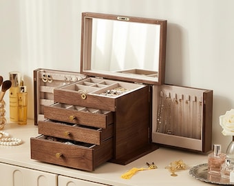 May include: A wooden jewelry box with multiple drawers and compartments. The box is open, revealing a mirror, drawers, and storage for necklaces and rings. The box is made of dark wood and has gold-colored hardware. The jewelry box is on a white surface.