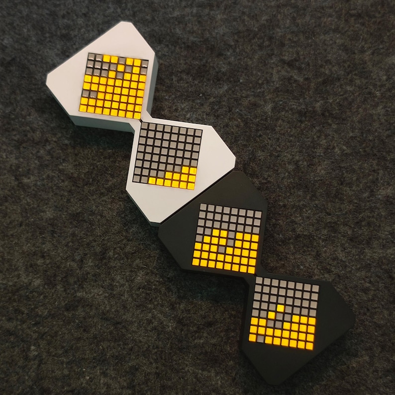 May include: Four geometric, modular LED light panels in a row. The panels are white and black, with a grid of small squares that light up in yellow and gray. The panels are arranged on a dark gray surface.