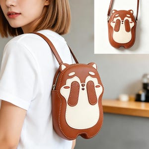 Peut inclure: Un sac bandoulière en cuir marron en forme de renard de dessin animé, avec des accents blancs et crème. Le sac est doté d'une fermeture éclair et d'une longue bandoulière. Le design du renard comprend des détails cousus et une expression ludique.