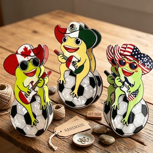 May include: Three whimsical frog figurines, each perched on a soccer ball, wearing sunglasses and playing guitars. One frog sports a Canadian flag hat, another a Mexican flag hat, and the third an American flag hat. The word "HANDMADE" is on a tag.