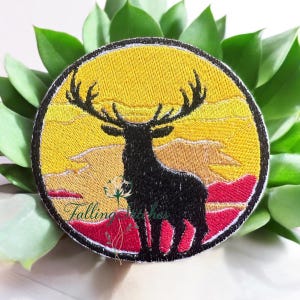 May include: Embroidered patch featuring a black silhouette of a stag against a yellow and orange sunset. The patch is circular with a black border and includes the text "Falling Stitches".