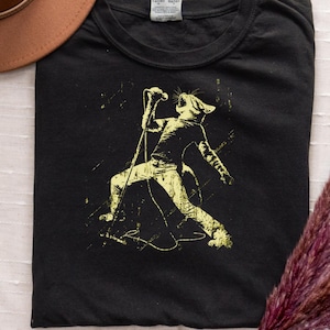 May include: Black t-shirt with a yellow graphic of a cat singing into a microphone. The cat is wearing trousers and a shirt, and is in a dynamic pose. The t-shirt is made of a soft material and is suitable for casual wear.