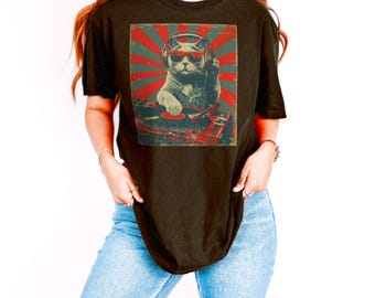 Puede incluir: Camiseta negra con un diseño gráfico retro de un gato con gafas de sol y auriculares, pinchando en un tocadiscos. El diseño utiliza colores rojo y verde. El gato es el foco principal del diseño, con un ambiente vintage.