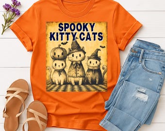 以下が含まれることがあります： ハロウィーンをテーマにしたグラフィックが特徴のオレンジ色のTシャツ。グラフィックには、ハロウィーンの衣装を着た3匹の漫画の猫と、その上に「Spooky Kitty Cats」というテキストが含まれています。シャツはブルージーンズとサンダルと組み合わせて表示されています。