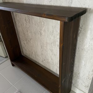 May include: A dark brown wooden console table with a rectangular top and a lower shelf. The table has a simple, open design and is made of solid wood. The finish is a rich, dark stain, and the table is approximately 122 cm long.
