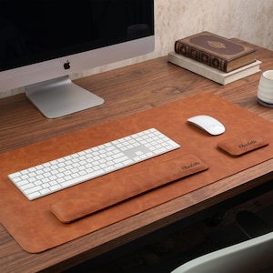 May include: A tan leather desk mat set featuring a large rectangular mat, a long keyboard wrist rest, and a small mouse wrist rest. Both wrist rests are embossed with the name Charlotte in a dark script font, providing a coordinated workspace.
