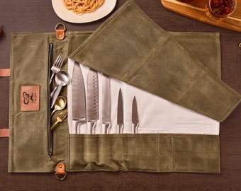 May include: An open olive green canvas knife roll with a variety of stainless steel knives and silverware. The roll is partially unrolled, revealing the knives and utensils. A leather patch with a logo is visible.