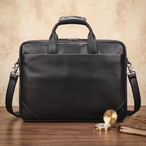 May include: A black leather briefcase featuring a top handle, a detachable shoulder strap with metal clips, and the name Diego embossed on the front. The bag has a rectangular shape with a smooth finish and a zippered main compartment closure.