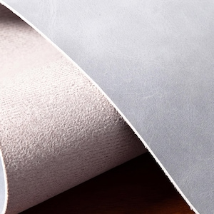 May include: A sheet of light gray material with a smooth, matte top surface and a textured, fibrous underside. The material is partially rolled, revealing the contrast between the flat, uniform exterior and the rough, porous interior structure.
