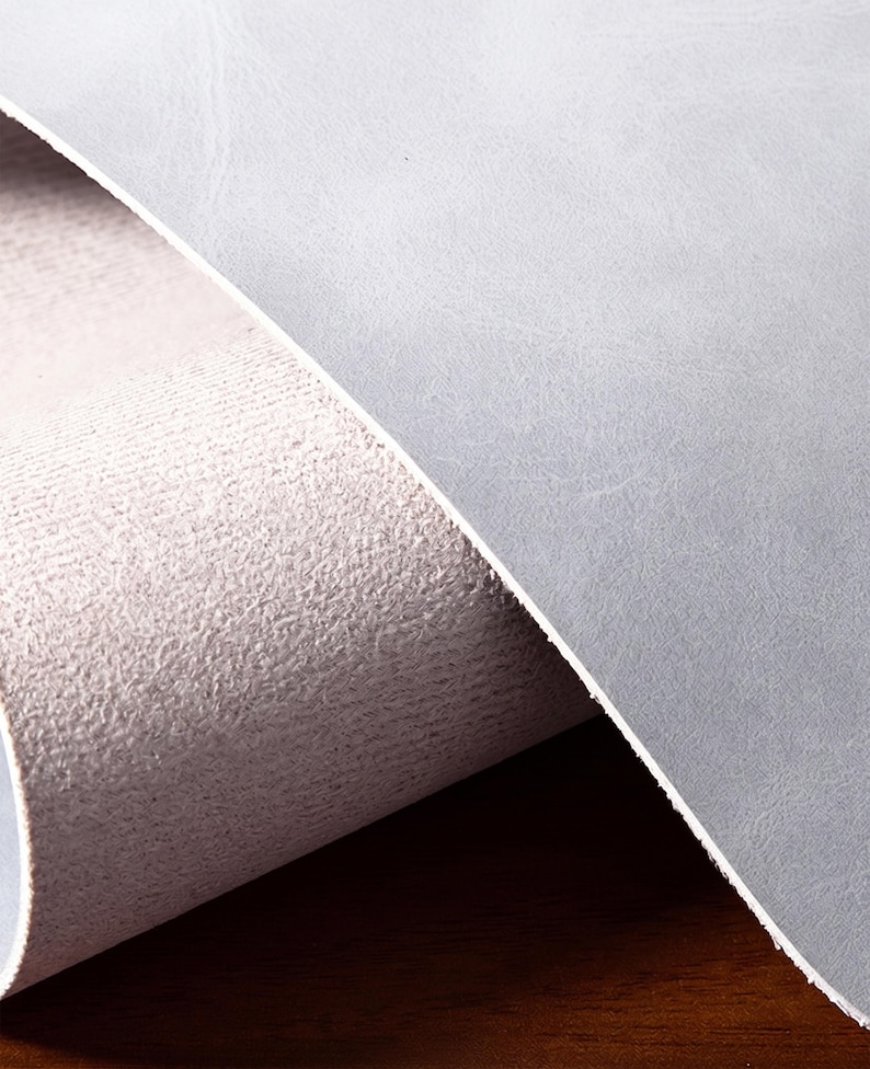 May include: A sheet of light gray material with a smooth, matte top surface and a textured, fibrous underside. The material is partially rolled, revealing the contrast between the flat, uniform exterior and the rough, porous interior structure.
