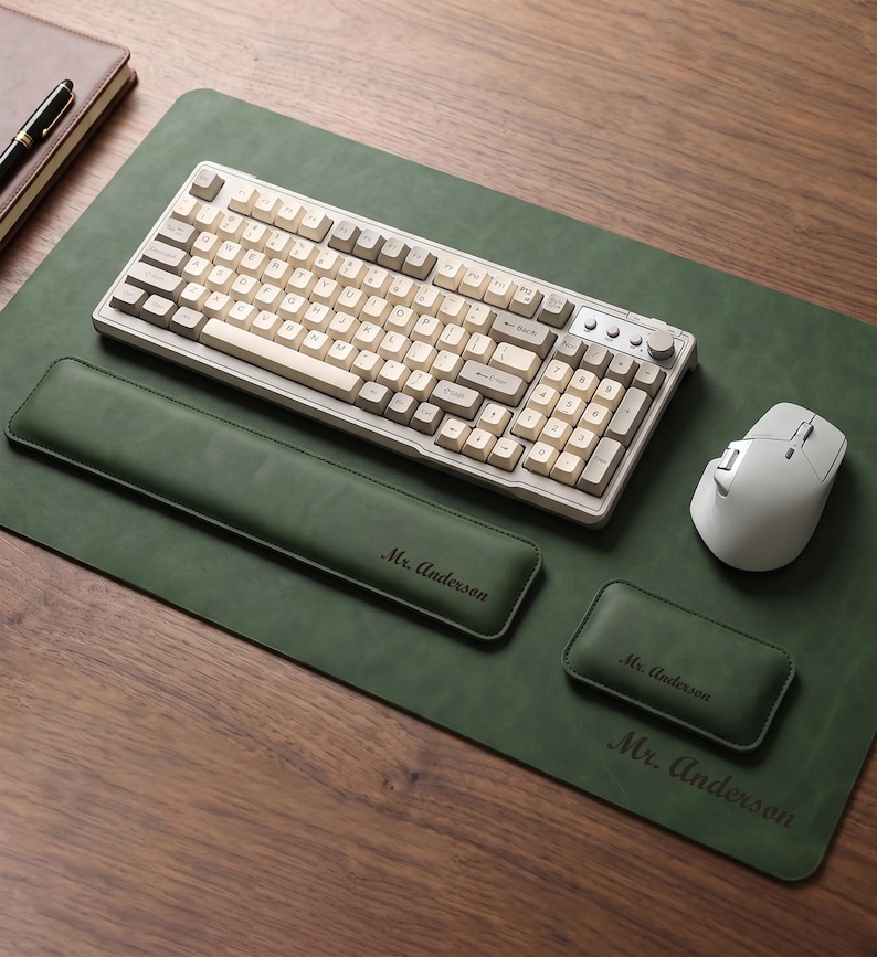 May include: A dark green desk mat with a matching wrist rest and mouse pad, all featuring the name Mr. Anderson. A mechanical keyboard with cream and grey keys and a white wireless mouse are placed on the mat, which has a smooth, matte finish.