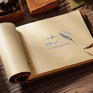 Op de afbeelding: Open notitieboek met bruine leren kaft en bruine pagina's. De woorden "music" en "infinite" zijn in cursief geschreven, samen met een veerillustratie. De zin "The rest is still unwritten" staat ook op de pagina.