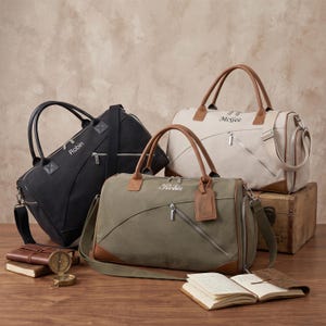 Op de afbeelding: Drie reistassen in zwart, olijfgroen en beige, elk voorzien van een diagonale rits, handvatten en een schouderriem. De zwarte tas is gepersonaliseerd met de naam Robin, de olijfgroene met Robin en de beige tas met McGee.