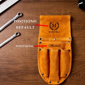 May include: A tan leather tool belt with multiple pockets and the name "Maxwell" engraved on it. The belt has a decorative "M" emblem and is shown with two spanners and a ruler on a wooden surface.