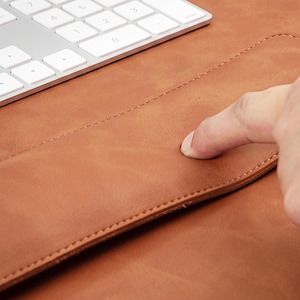 May include: A tan leather desk mat with a smooth, matte surface and stitched edges, positioned next to a white wireless computer keyboard with a numeric keypad. The material shows a natural grain texture and a soft, flexible appearance.