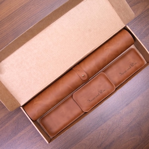 May include: A tan leather set inside a cardboard box, including a cylindrical roll with a strap, a rectangular case, and a small rectangular tag. The case and tag are both embossed with the text Focus and Win in a dark script font.