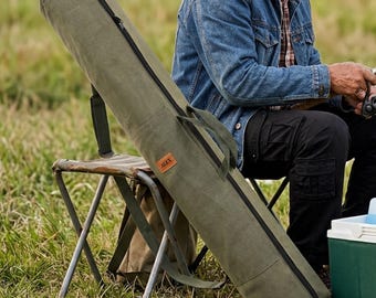 May include: An olive green canvas fishing rod bag with a long black zip closure, two fabric carrying handles, and a small rectangular brown leather patch featuring the text ALEX embossed in the centre of the exterior side panel.