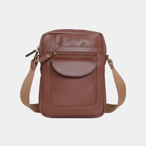 May include: A brown leather crossbody bag with a rectangular shape. It features a front pocket with a curved flap, a zippered top, and a tan adjustable shoulder strap. The bag is designed for carrying essentials.