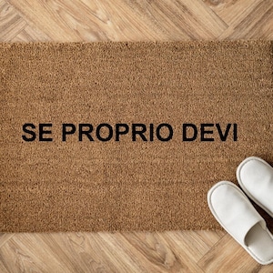 Può includere: Un zerbino rettangolare marrone in fibra di cocco con la scritta "SE PROPRIO DEVI" in nero. Due pantofole bianche sono posizionate a destra del tappeto. Lo zerbino è su un pavimento in legno.