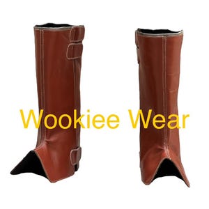 May include: A pair of brown leather boots with a knee-high design. The boots have two buckles on the side and white stitching. The text "Wookiee Wear" is displayed in yellow across the image.