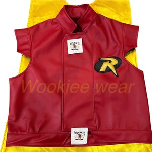 Può includere: Un gilet rosso con un emblema nero e giallo e un mantello giallo. Il gilet ha un colletto alto e maniche corte. Il testo "Wookiee wear" è visibile sul gilet.