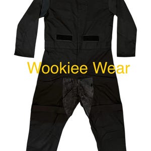 May include: Black jumpsuit with long sleeves, a collared neckline, and multiple pockets. The text "Wookiee Wear" is displayed in yellow across the front. The jumpsuit has a dark, textured panel on the lower front.
