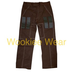 May include: Brown pants with white stitching and four rectangular patches on the front. The text "Wookiee Wear" is printed in yellow across the bottom of the image. These pants are likely part of a costume.