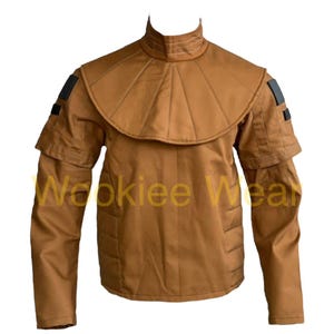 May include: A tan-colored jacket with a high collar and layered shoulder design. The jacket features a unique, structured collar and shoulder detailing, with black accents on the sleeves. The text "Wookiee Wear" is printed on the front.