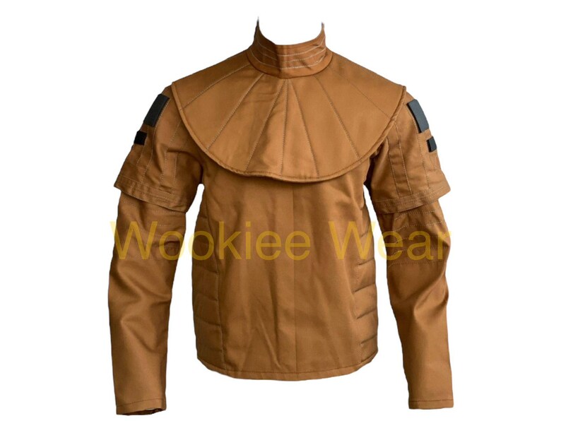 May include: A tan-colored jacket with a high collar and layered shoulder design. The jacket features a unique, structured collar and shoulder detailing, with black accents on the sleeves. The text "Wookiee Wear" is printed on the front.