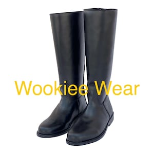 Può includere: Un paio di stivali neri al ginocchio. Gli stivali sono realizzati in un materiale liscio e hanno un design classico. Il testo "Wookiee Wear" è visualizzato in giallo sull'immagine.