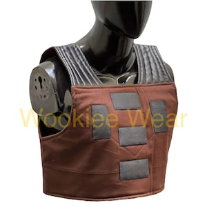 May include: Brown vest with black detailing, displayed on a black mannequin. The vest has a rectangular design with several black patches and a textured shoulder area. The text "Wookiee Wear" is visible in yellow.