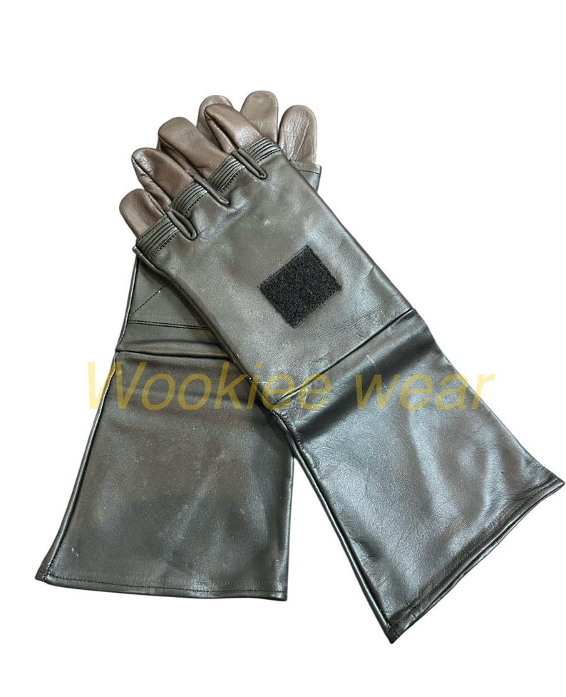 Pu&ograve; includere: Un paio di guanti in pelle nera con punte delle dita marroni e una toppa in velcro nera. I guanti hanno polsini lunghi. Il testo "Wookiee Wear" &egrave; visibile. Guanti protettivi.
