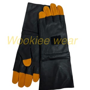 Pu&ograve; includere: Guanti neri con punte delle dita arancioni e una toppa nera. I guanti hanno polsini lunghi e sono realizzati in un materiale liscio. Il testo "Wookiee wear" &egrave; visibile in basso a sinistra.