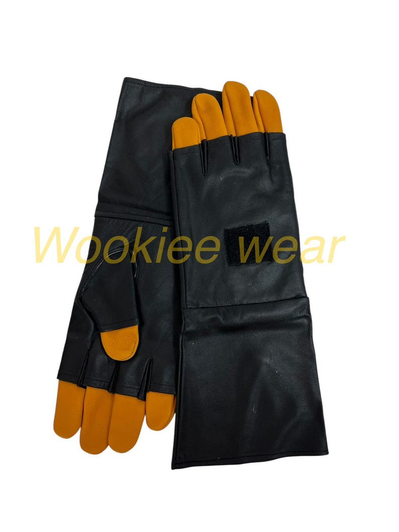 Pu&ograve; includere: Guanti neri con punte delle dita arancioni e una toppa nera. I guanti hanno polsini lunghi e sono realizzati in un materiale liscio. Il testo "Wookiee wear" &egrave; visibile in basso a sinistra.