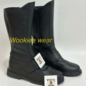 Può includere: Un paio di stivali in pelle nera con gambale alto e chiusura a zip. Gli stivali hanno un cinturino sulla parte superiore del piede e il testo "Wookiee wear" è visibile. Due etichette bianche con un logo sono attaccate.