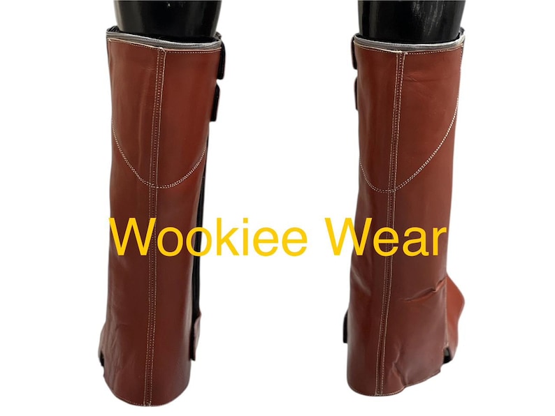 May include: Pair of brown leather boots with white stitching and black buckles. The boots have a silver trim at the top and the text "Wookiee Wear" in yellow.