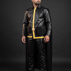 May include: A black faux leather long-sleeve jacket with a yellow vertical stripe, matching black trousers, and a long black cape. The outfit includes a black utility belt with a gold-toned buckle and two attached black pouches on the front.