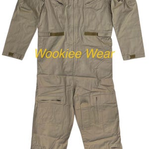May include: A tan-coloured jumpsuit featuring a zip closure, multiple pockets, and a Ghostbusters logo patch on the left shoulder. The text "Wookiee Wear" is printed across the front. This one-piece garment is suitable for cosplay or costume events.
