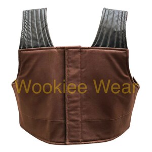 May include: Brown vest with black shoulder straps. The vest has a rectangular shape with a vertical seam down the front. The text "Wookiee Wear" is printed in gold on the front of the vest.