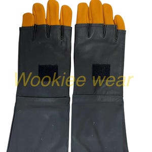 Pu&ograve; includere: Un paio di guanti neri con coperture arancioni per le dita e il pollice. I guanti hanno un polsino lungo e una piccola toppa quadrata nera sul dorso della mano. Il testo "Wookiee wear" &egrave; stampato sui guanti.