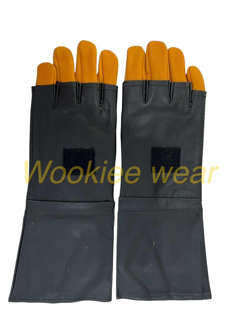 Pu&ograve; includere: Un paio di guanti neri con coperture arancioni per le dita e il pollice. I guanti hanno un polsino lungo e una piccola toppa quadrata nera sul dorso della mano. Il testo "Wookiee wear" &egrave; stampato sui guanti.