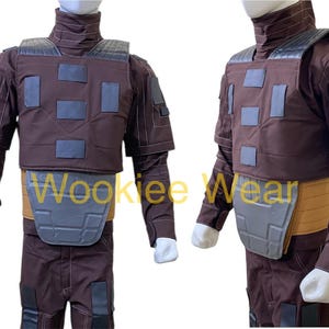 May include: A brown costume with a high collar, shoulder pads, and a chest plate. The costume has a tan belt and gray accents. The sleeves are long and the pants are brown. The costume is displayed on a mannequin.