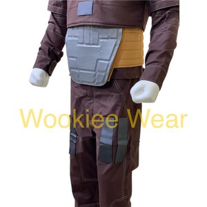May include: A brown costume with a gray chest plate and tan accents. The costume has a brown jacket and pants with black accents. The text "Wookiee Wear" is visible in yellow.