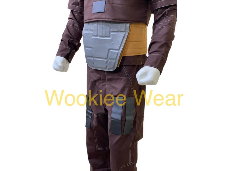 May include: A brown costume with a gray chest plate and tan accents. The costume has a brown jacket and pants with black accents. The text "Wookiee Wear" is visible in yellow.